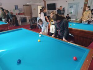 Une fille joue au billard sous le regard attentif de sa camarde